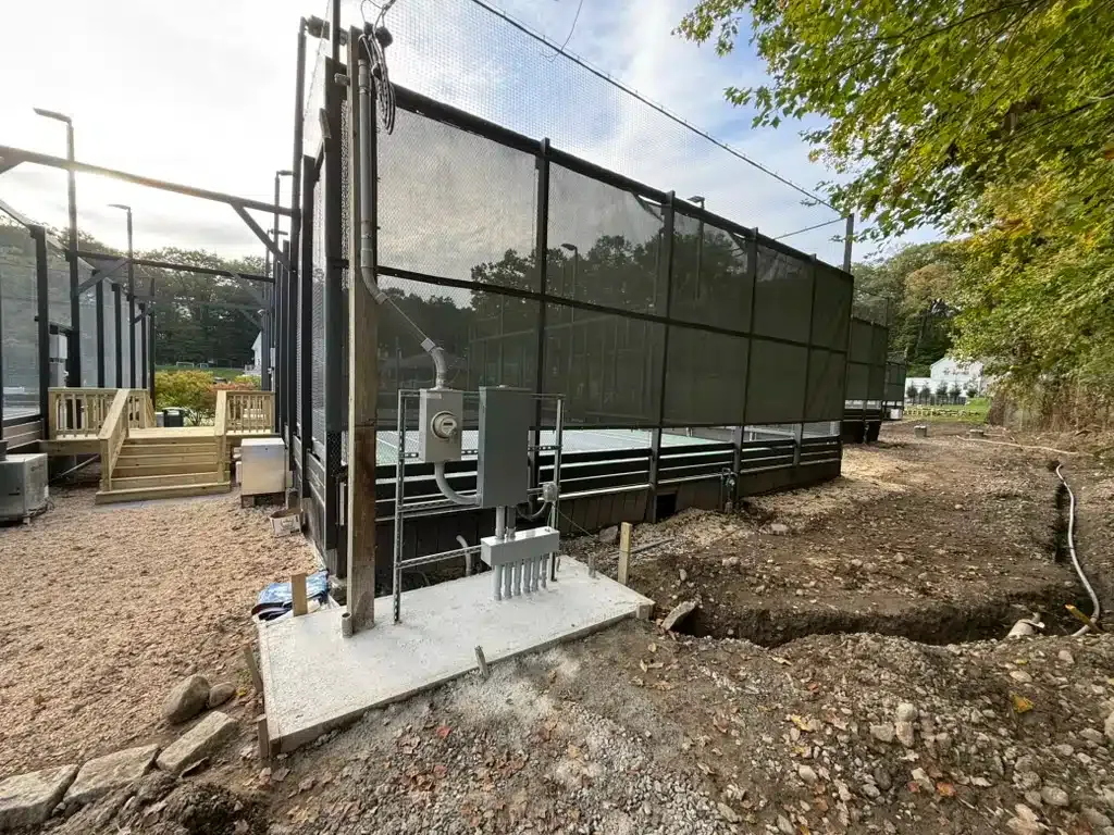 Outdoor pickleball court under construction with dark fencing and electrical box.