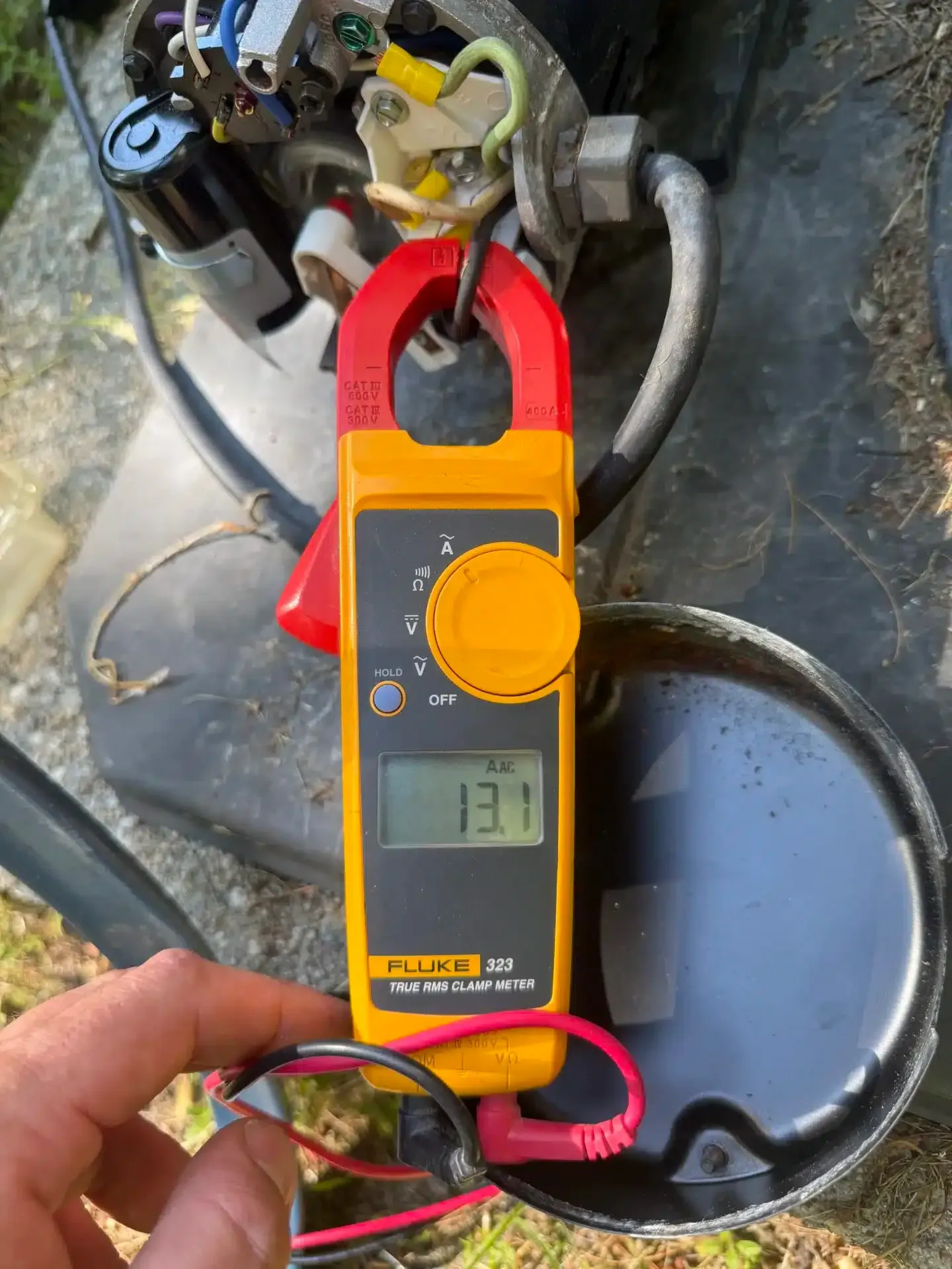 A clamp meter displaying 13.1 amps is clamped around a wire on an air compressor.