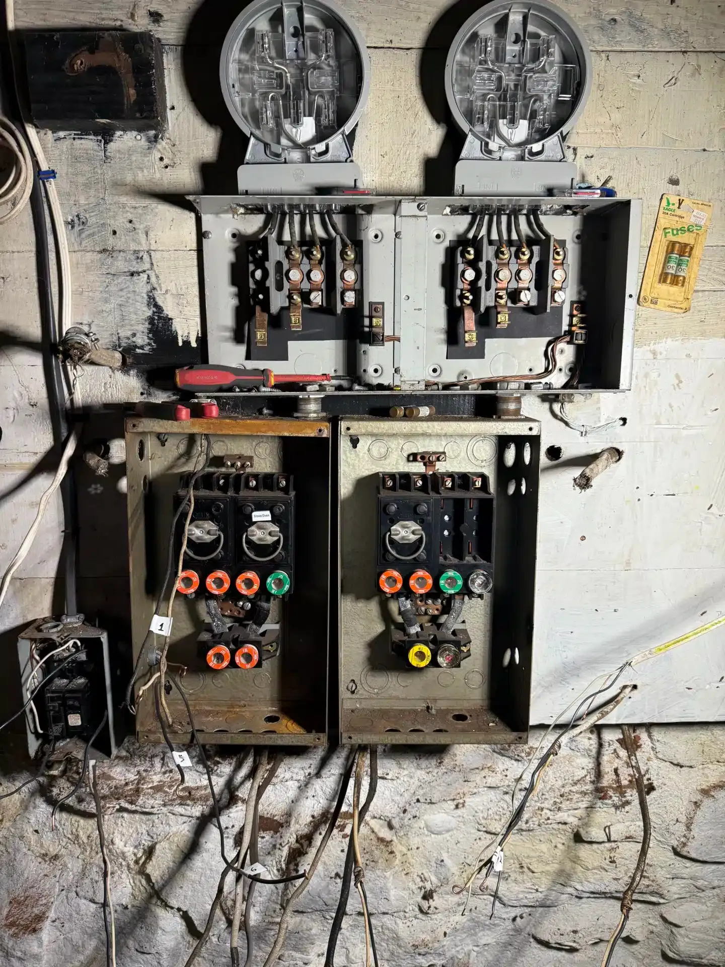 Electrical meters and circuit breakers mounted on a concrete wall with exposed wiring.