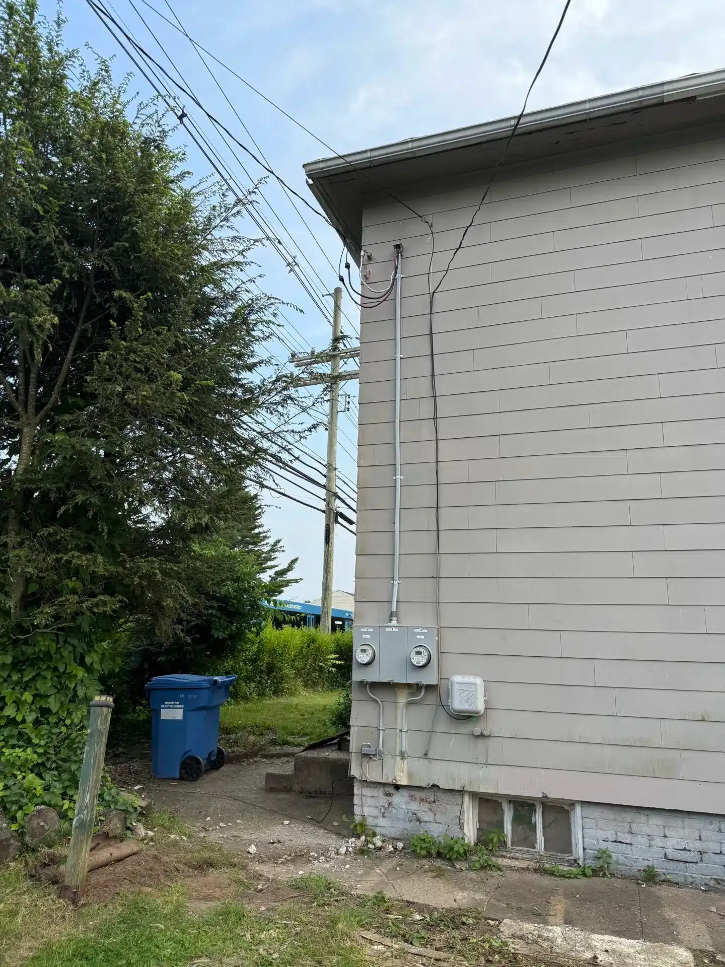 Exterior of a building with electrical meters, a utility pole, and power lines against a cloudy sky.