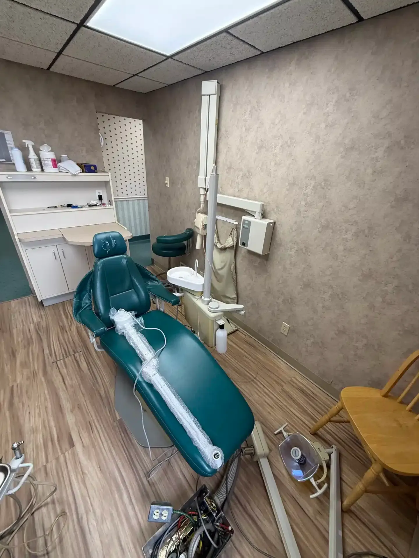 Dental examination room with a green chair, tools, and a wooden floor.