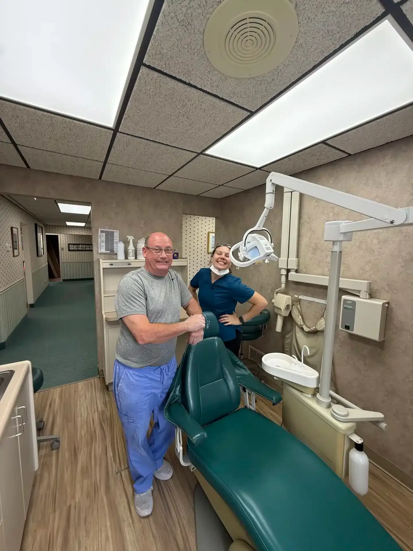 Two people in a dentist's office. One stands by a dental chair, the other leans against it.