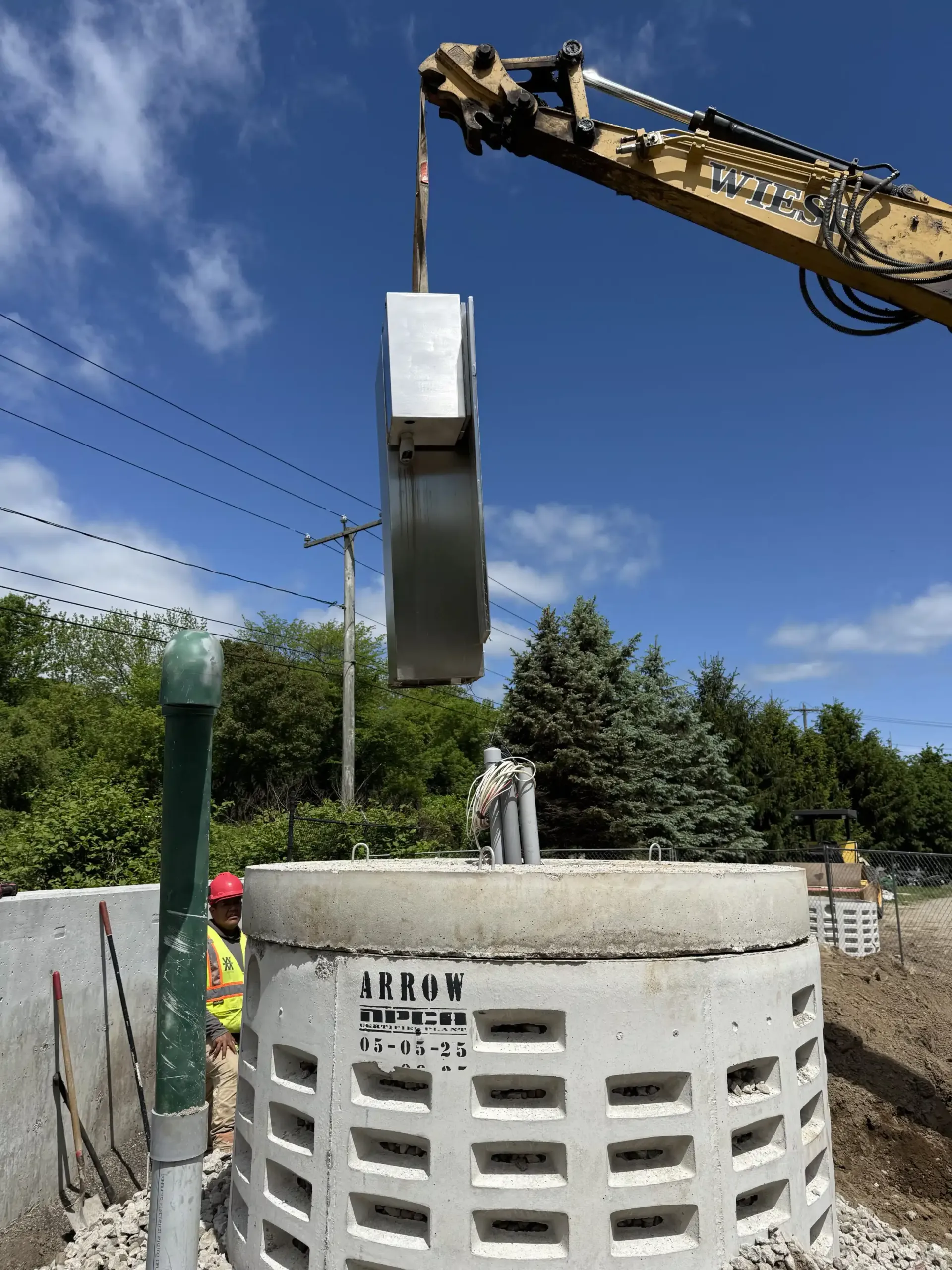 A construction site with a crane lifting a metal object over a concrete structure. Blue sky in the background.
