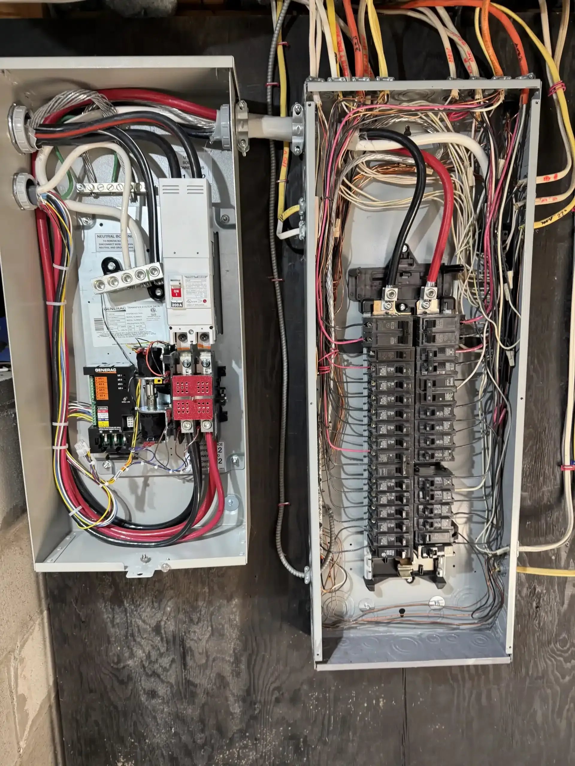 Two open electrical panels mounted on a wall; wires and breakers are visible inside the metal enclosures.