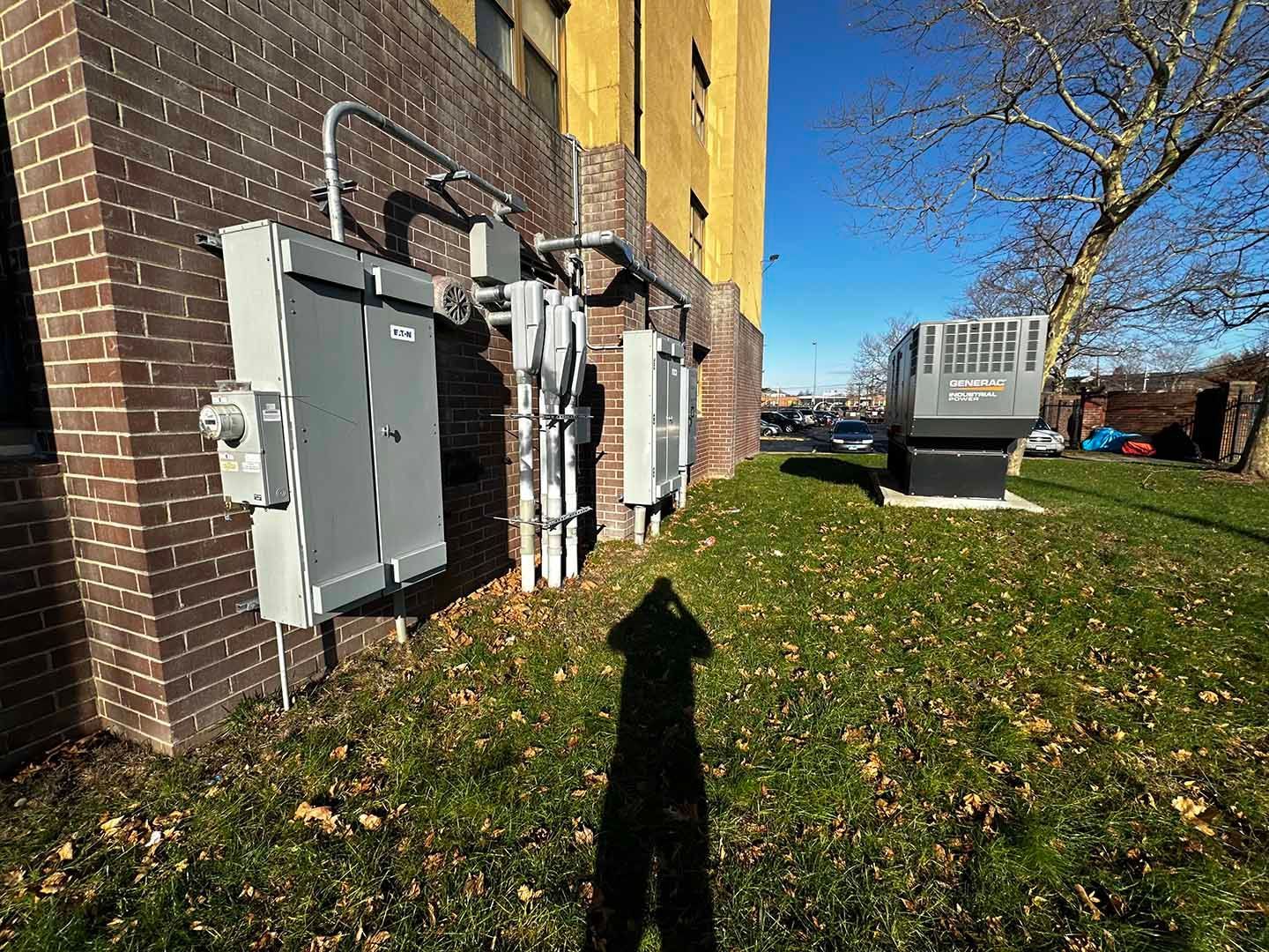 Electrical boxes and HVAC unit outside brick building on grassy lawn. Sunny day.