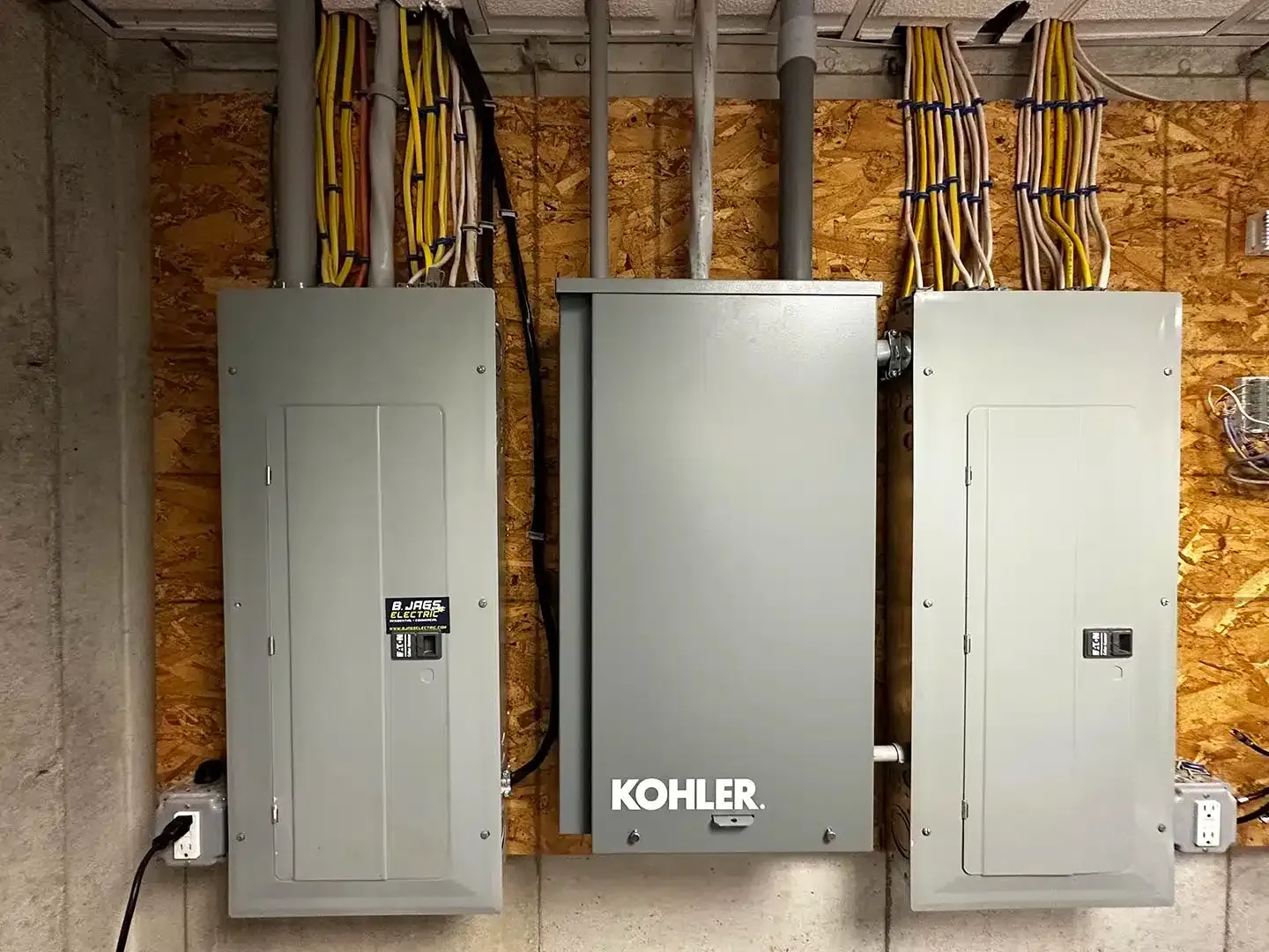 Electrical panels and a Kohler generator on a wood-paneled wall, with wiring overhead.