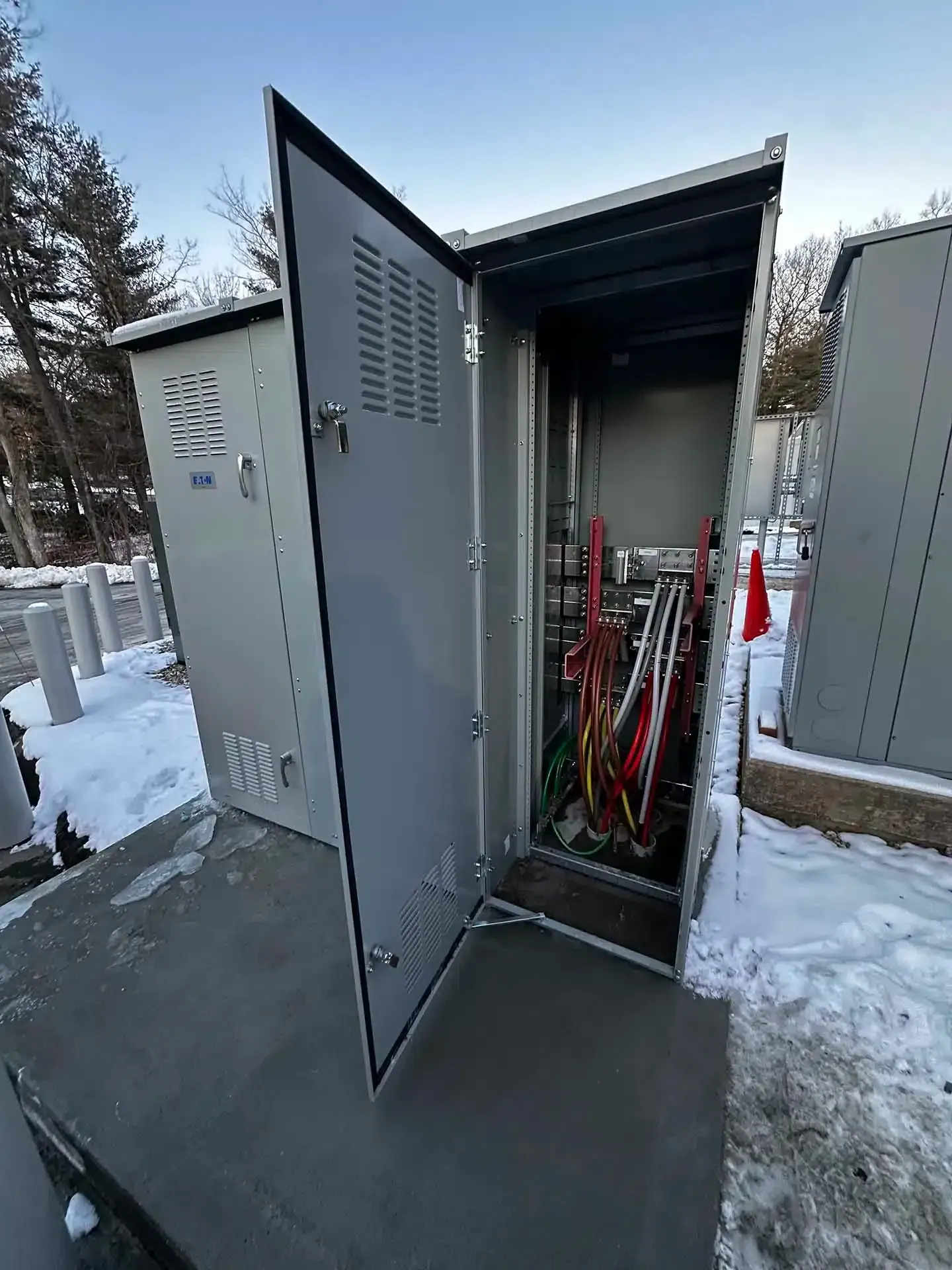 Metal electrical cabinet with open door, showing wires. Outdoors in a snowy environment.