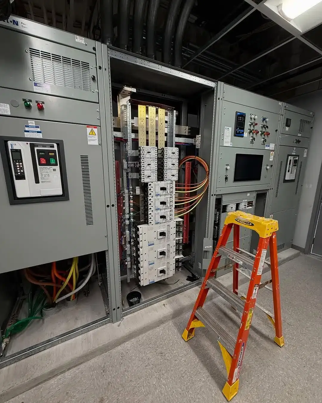 Electrical equipment cabinet with open door and a ladder in an indoor setting.