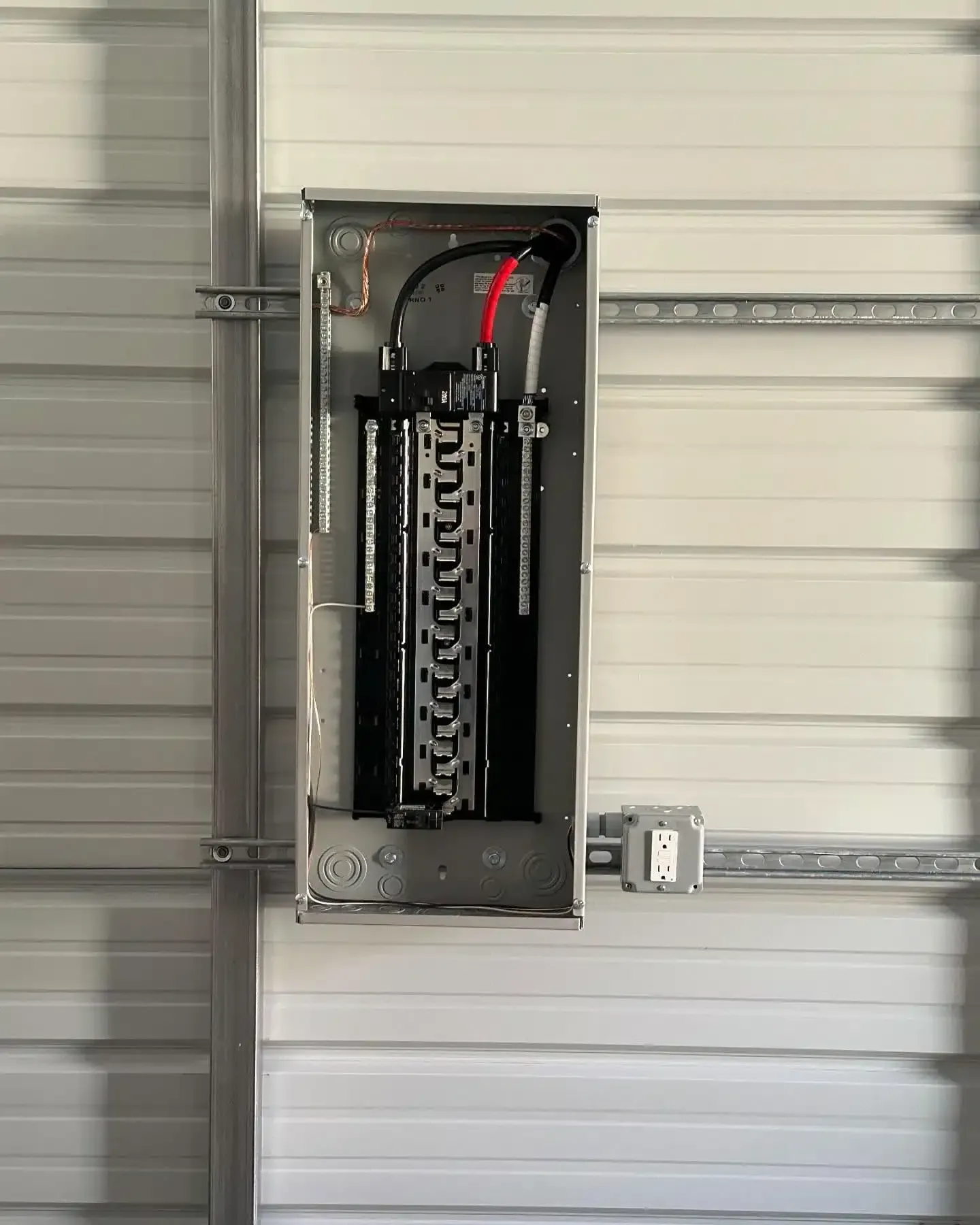 Electrical panel mounted on a metal wall, with exposed breakers and wiring.