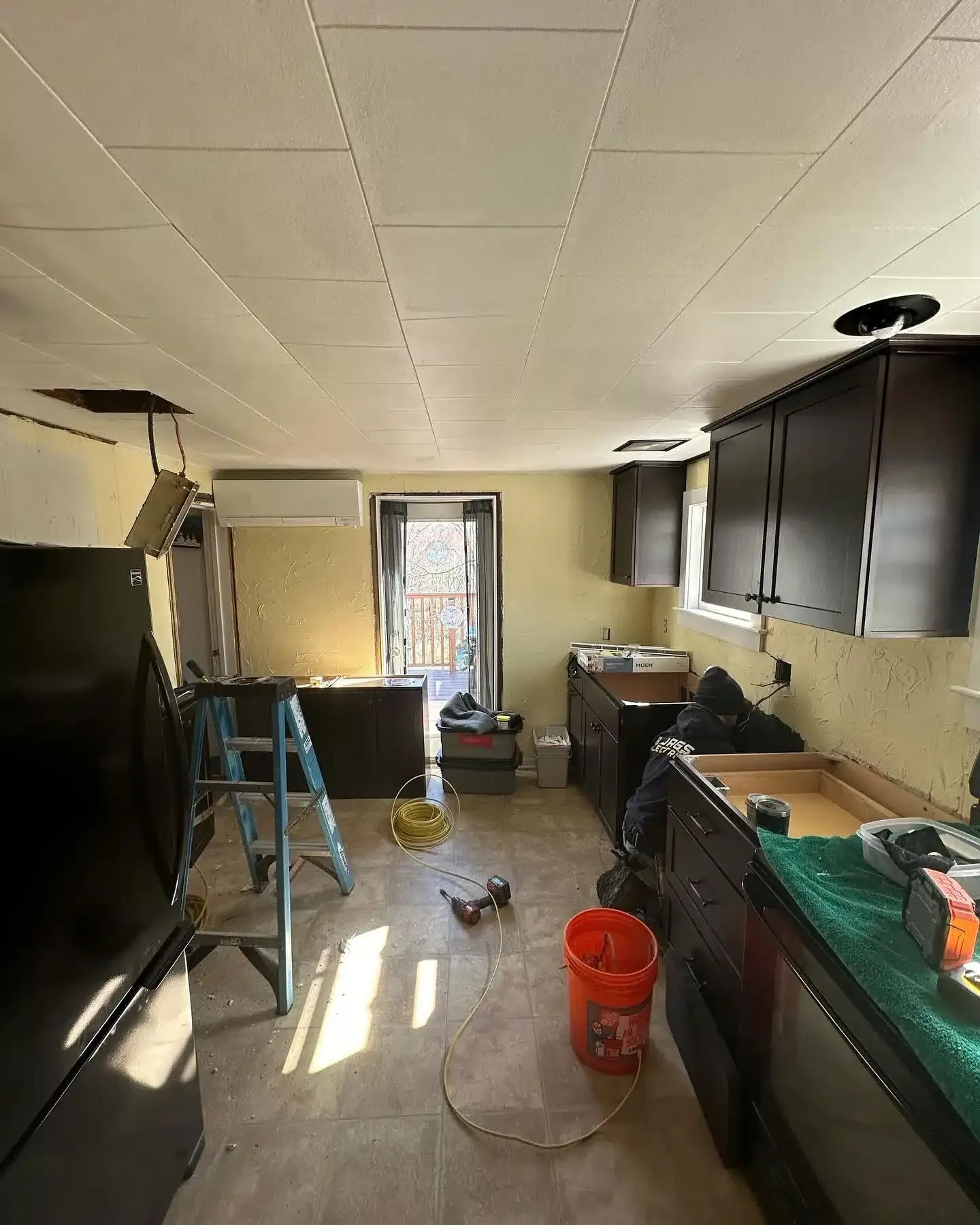 Kitchen under renovation with dark cabinets, exposed ceiling, and tools.