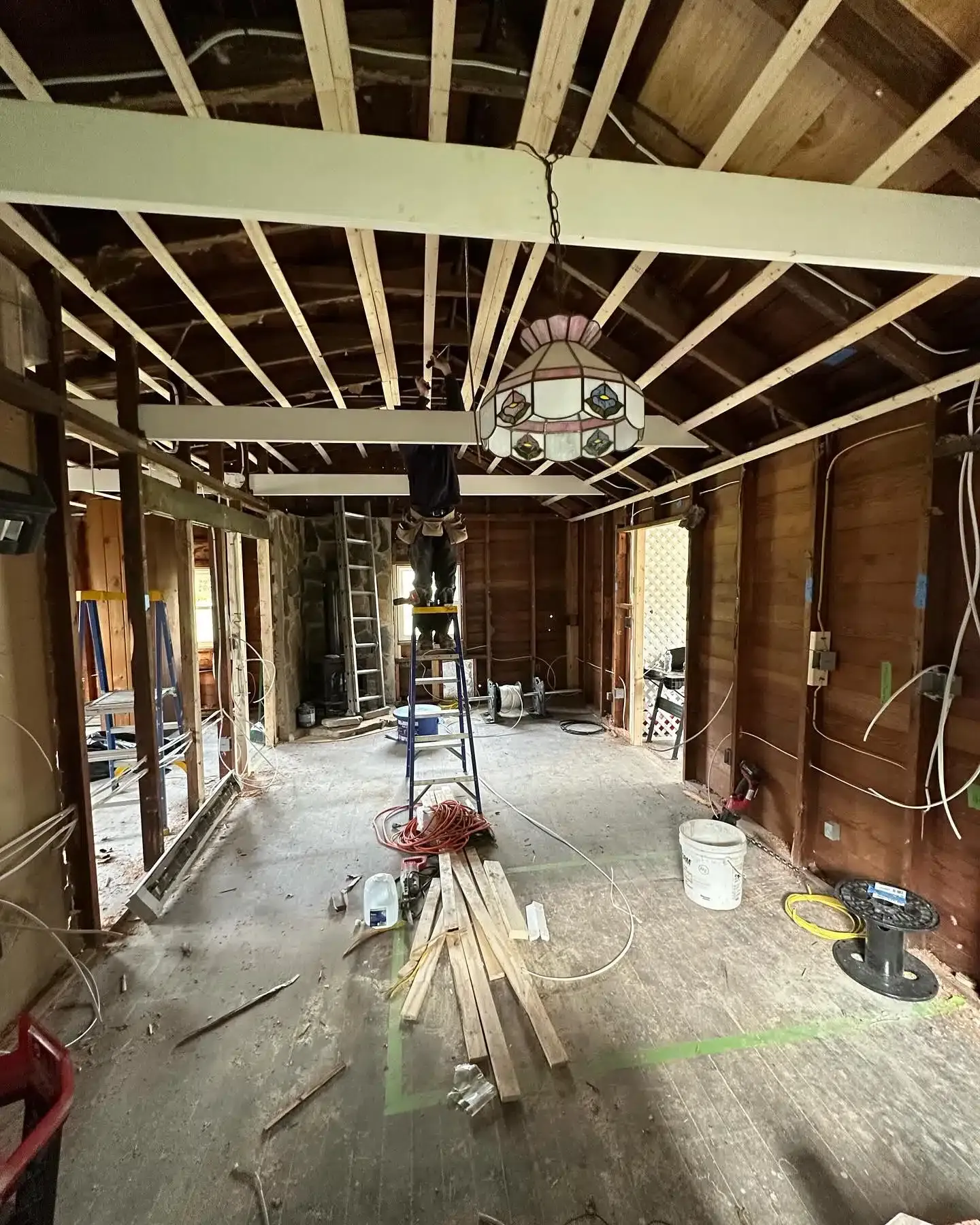 Interior of a house under renovation, exposed beams, bare wood walls, tools and debris scattered on the floor.