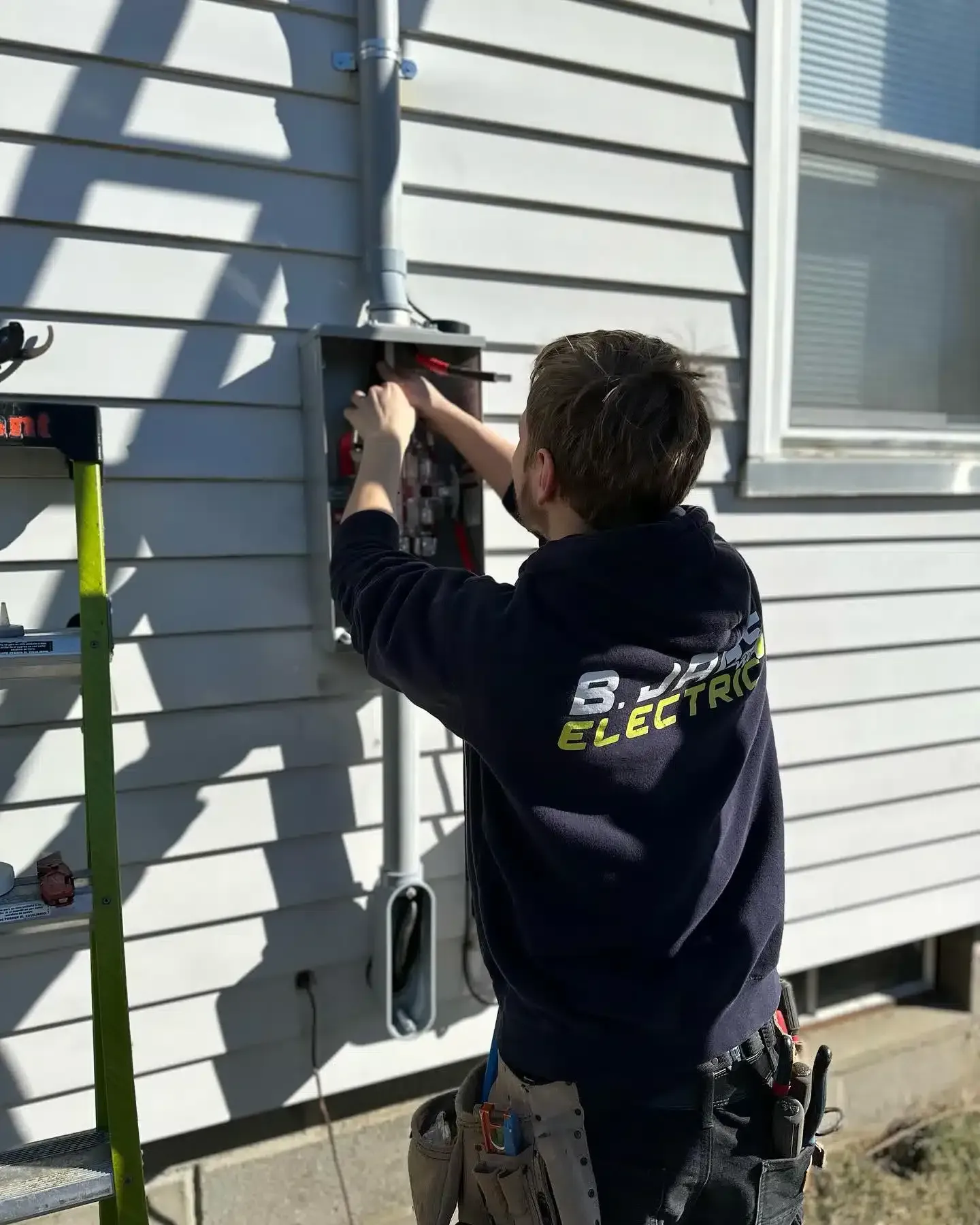 Electrician working on electrical panel mounted on a house exterior.
