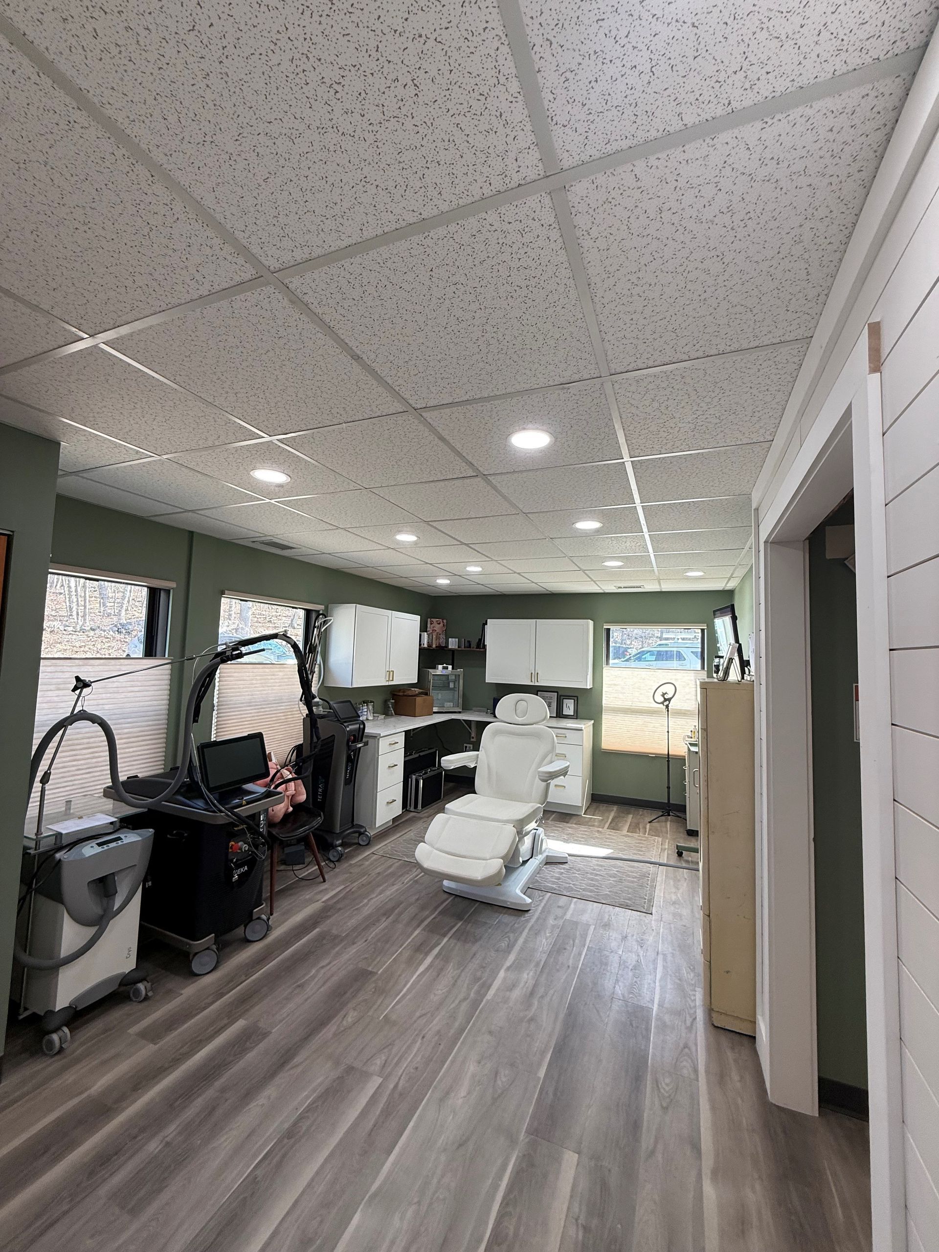A medical aesthetic room with wood-look floors, a white treatment chair, cabinetry, and equipment.