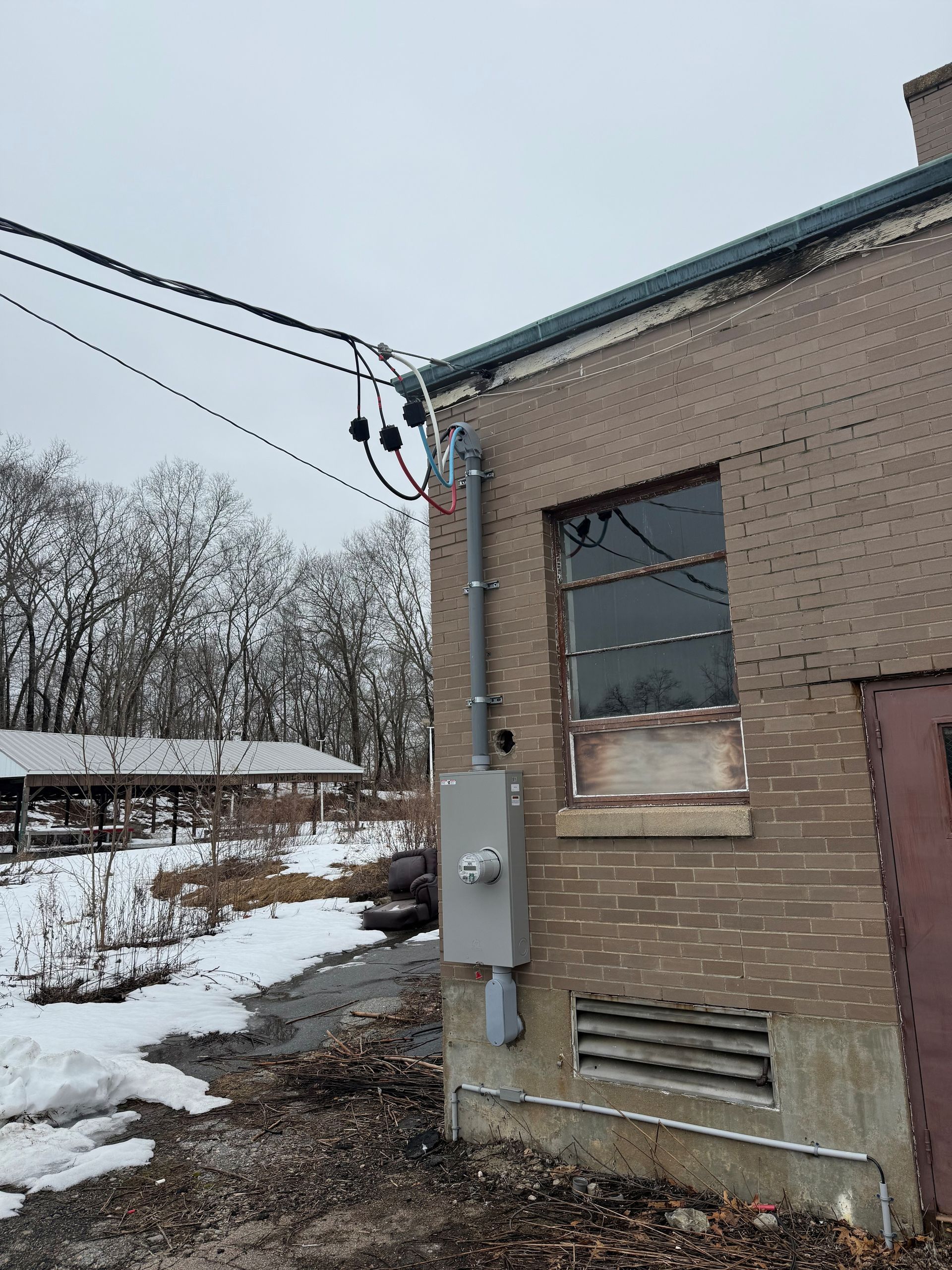 An outdoor electrical service entrance with a meter box and conduit mounted on a brick wall near a window.