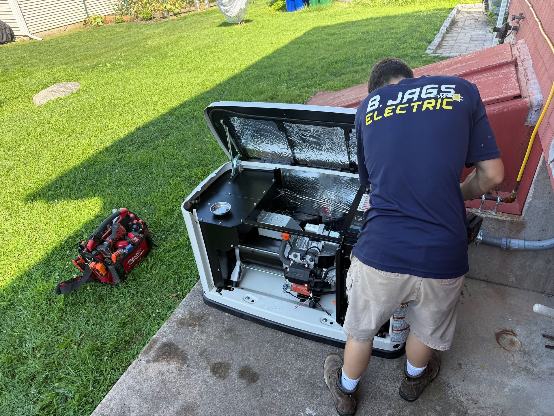 Technician in navy shirt works on open HVAC unit beside a house with tools on the lawn.