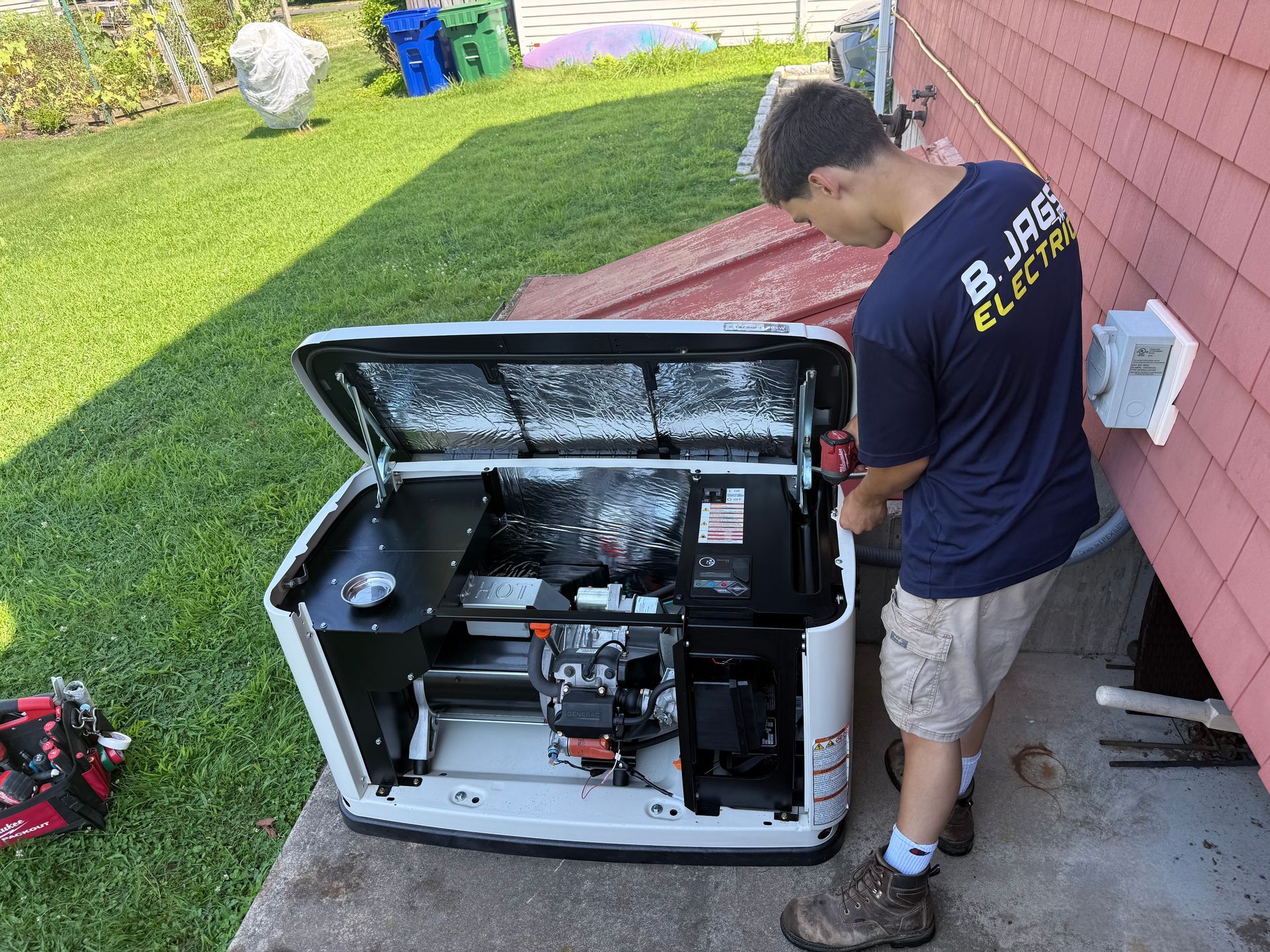 Man standing beside an open generator near a house, inspecting its interior.