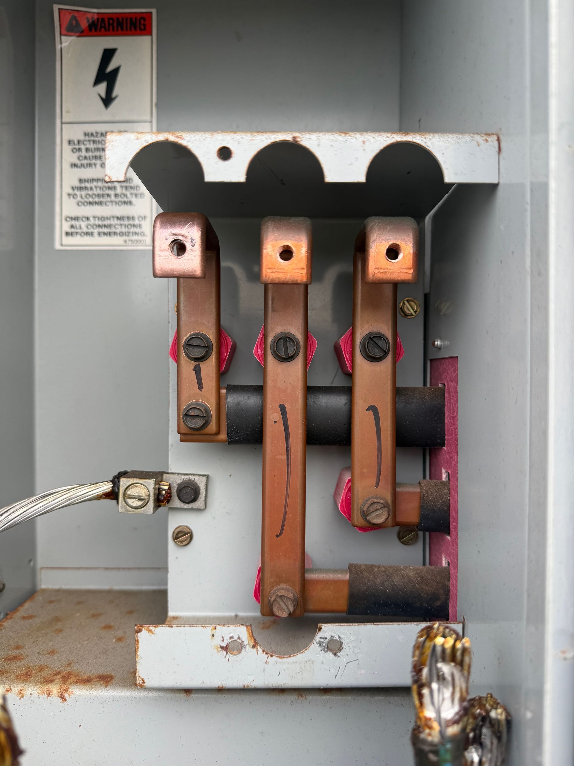 Open electrical panel with copper bus bars and warning label inside a gray metal box