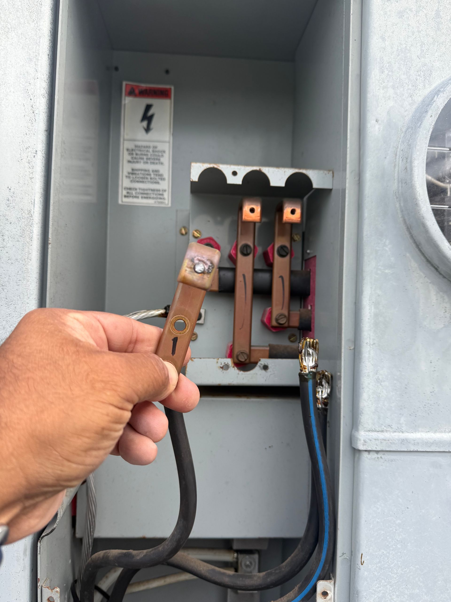 Hand holding a frayed electrical wire near an open breaker panel with exposed components