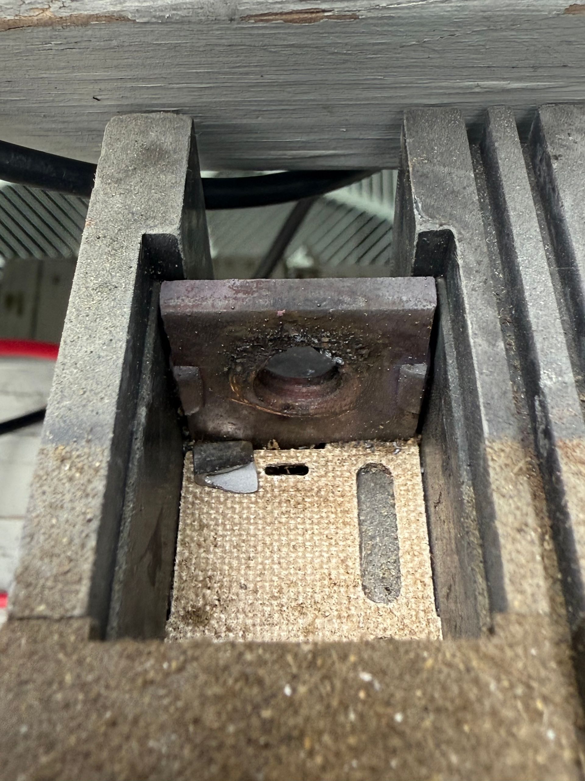 Close-up of a rusted metal bracket on a wooden surface with a central bolt and slotted holes.