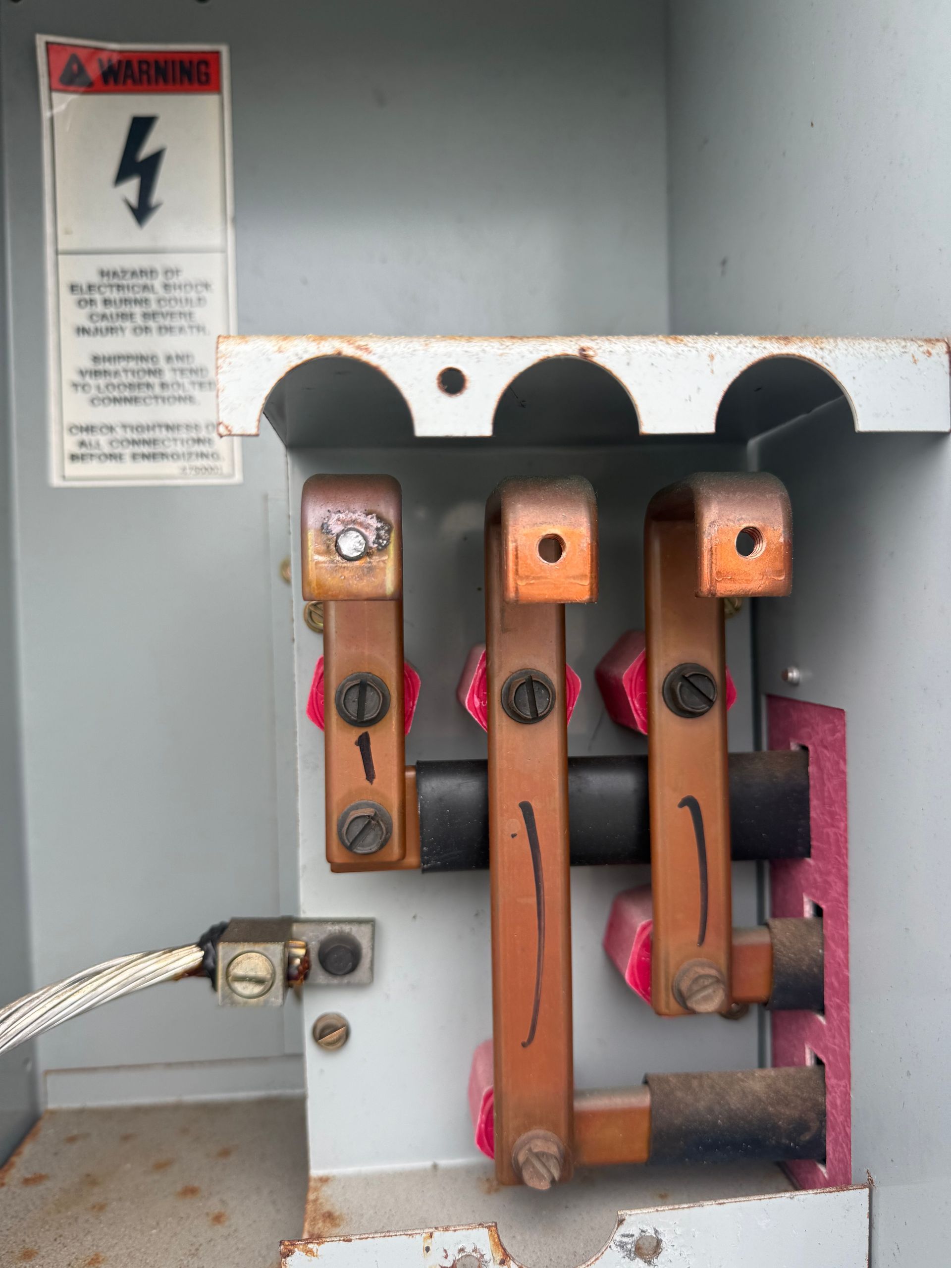 Open electrical panel with exposed copper bus bars and wires inside a gray metal cabinet.
