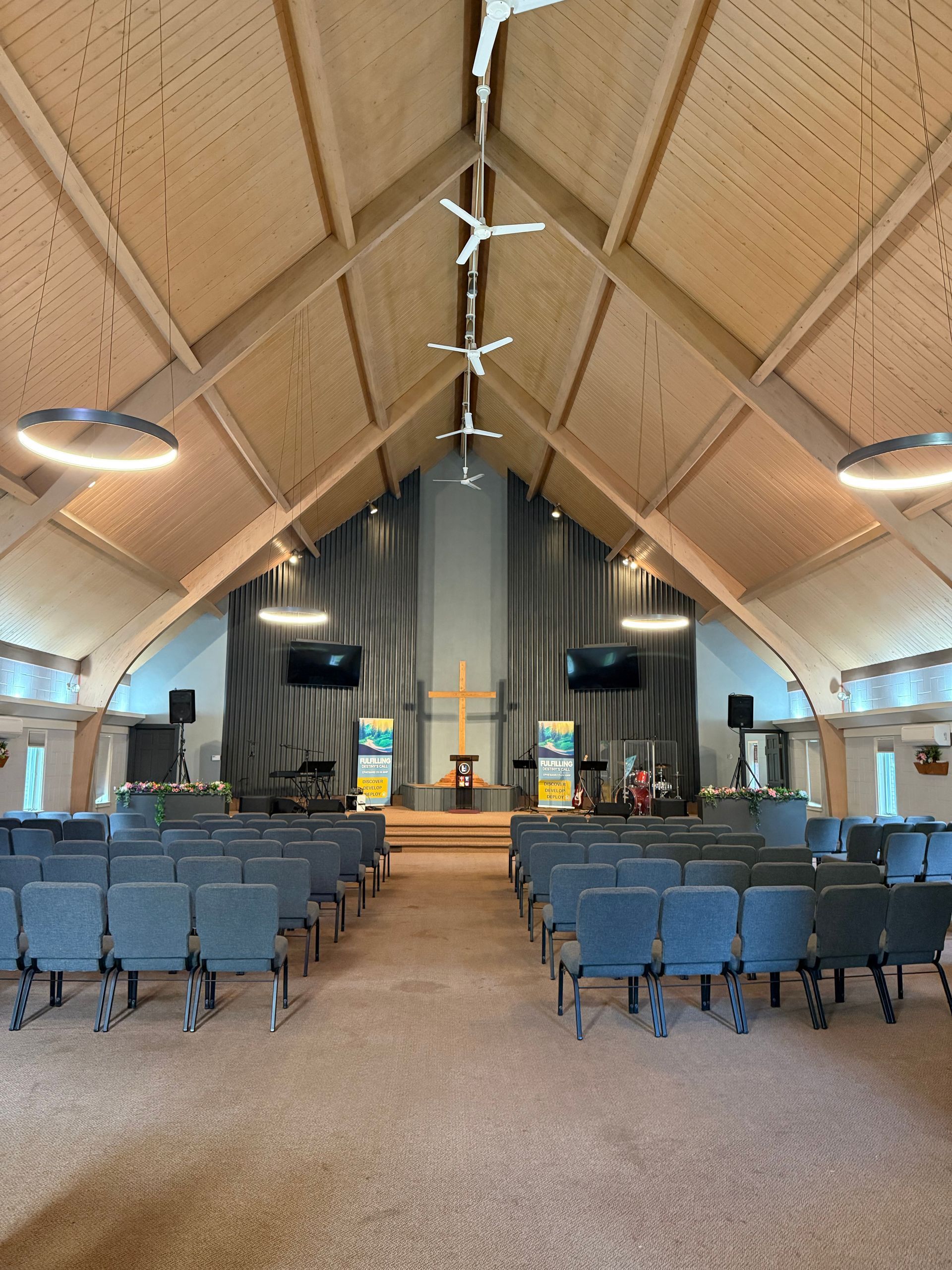 Wide-angle view of a church sanctuary with rows of blue chairs, a central aisle, and a high vaulted ceiling.