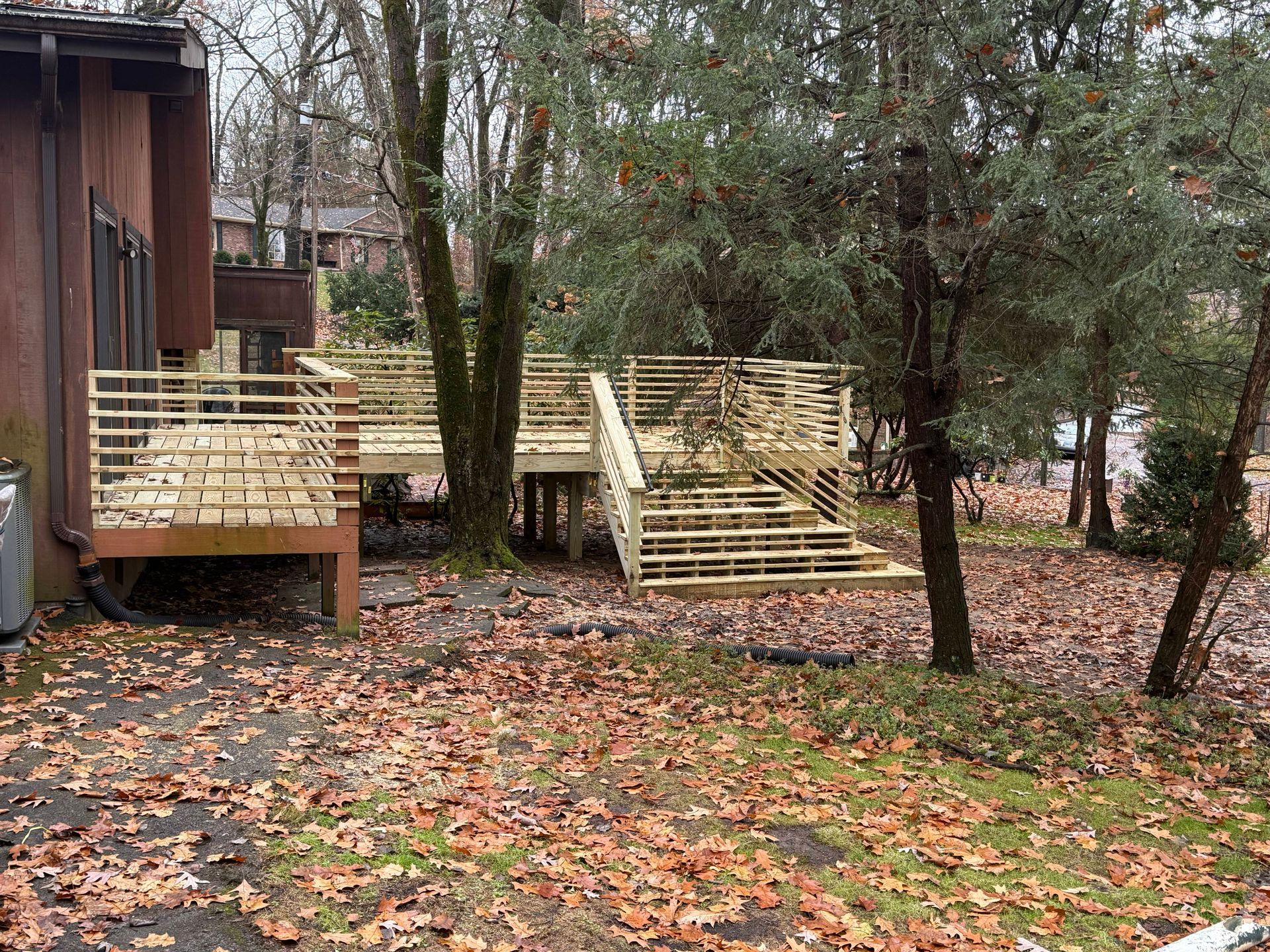 Newly constructed wooden deck with railings, set among trees and fallen leaves.