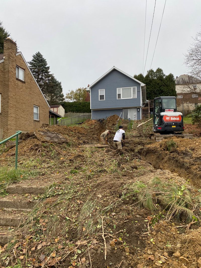 A man is digging in a dirt field in front of a house.