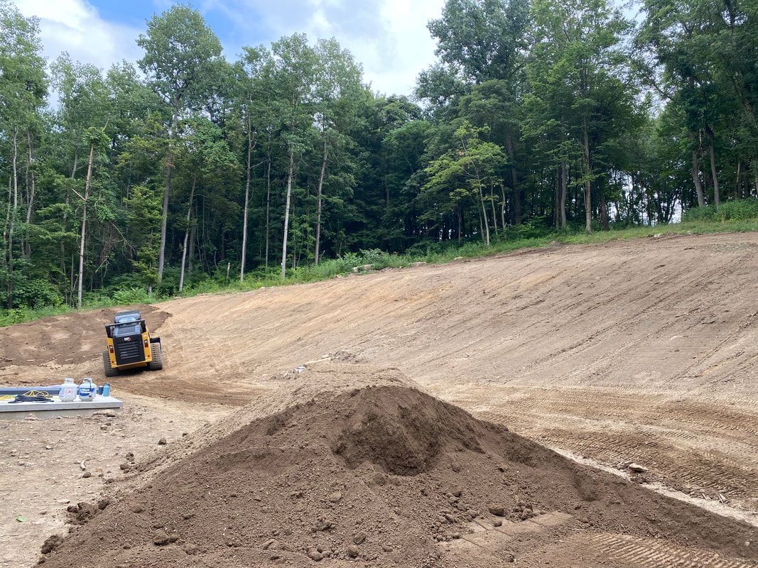 A bulldozer is driving down a dirt hill next to a pile of dirt.