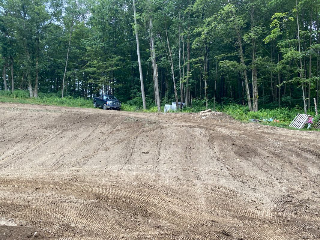 A truck is driving through a dirt field with trees in the background.