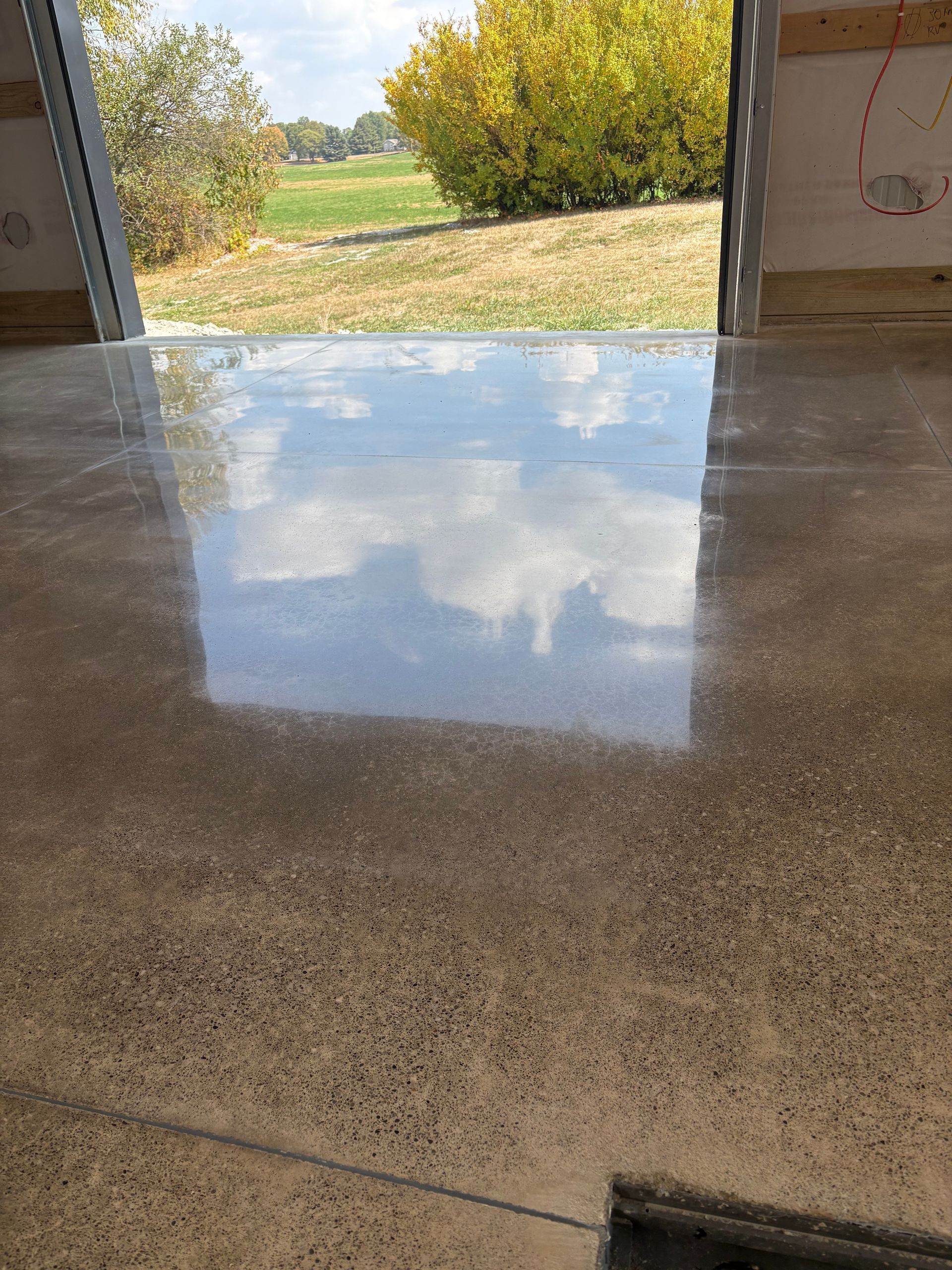 Polished concrete floor reflecting the sky and a doorway to a grassy outdoor area.