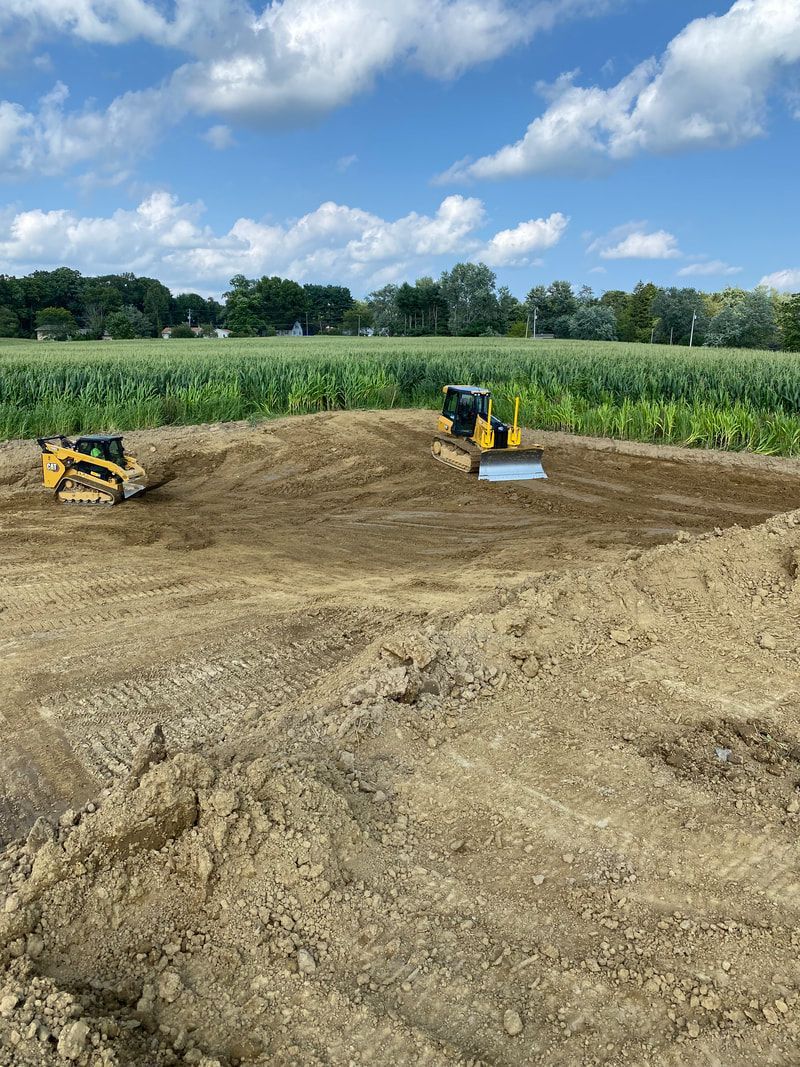 Two bulldozers are working on a dirt field.