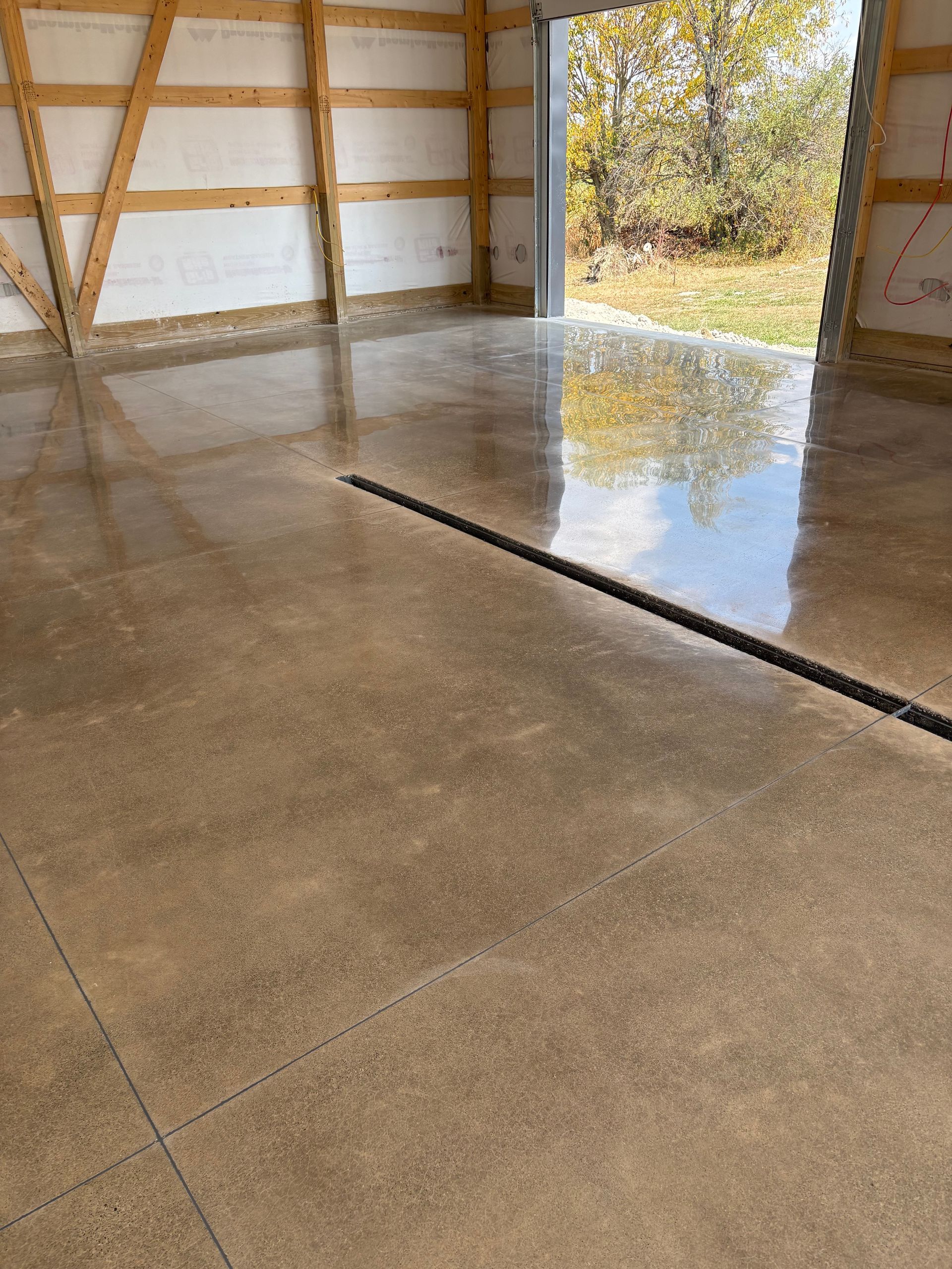 Polished concrete garage floor with a black drain, the open doorway shows the outdoors.