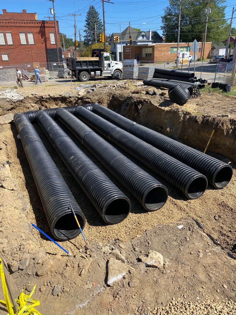A bunch of black pipes are stacked on top of each other in the dirt.