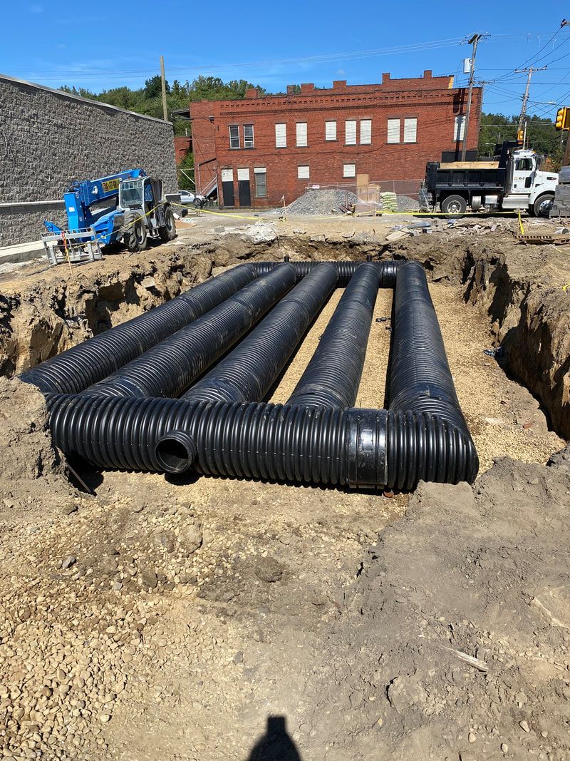 A large pile of pipes is sitting in the dirt in front of a brick building.