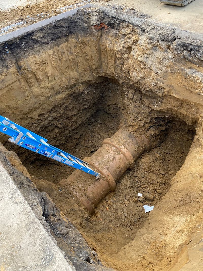 A large pipe is laying in the dirt in a hole.