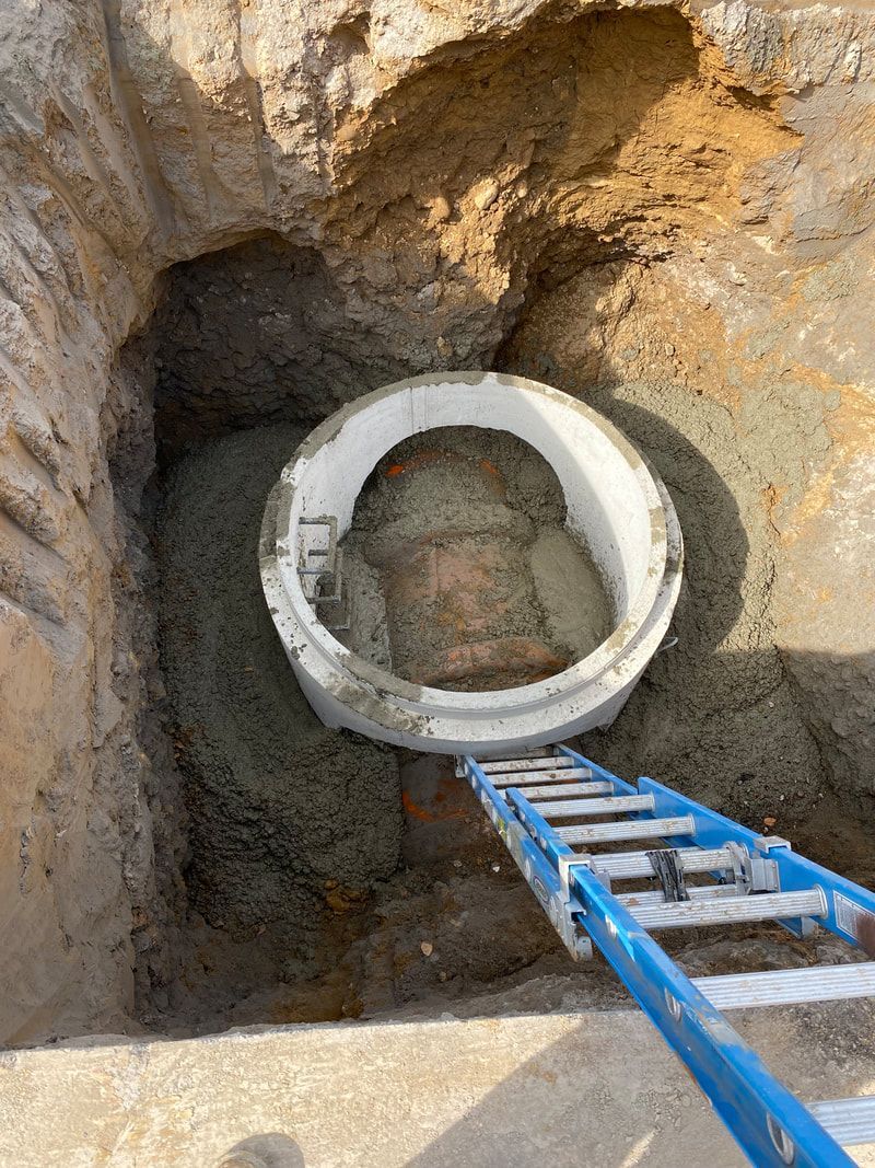 A ladder is going up to a concrete ring in a hole.
