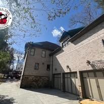 A sunny exterior view of a multi-story house with brick siding, a stone base, a three-car garage, and a driveway.