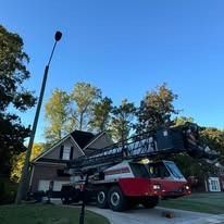 A red and white crane truck is parked in a residential driveway in front of a house, with its boom extended upward.