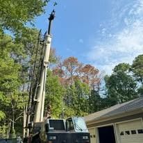 A white mobile crane extended into the sky beside a garage on a sunny day with trees in the background.