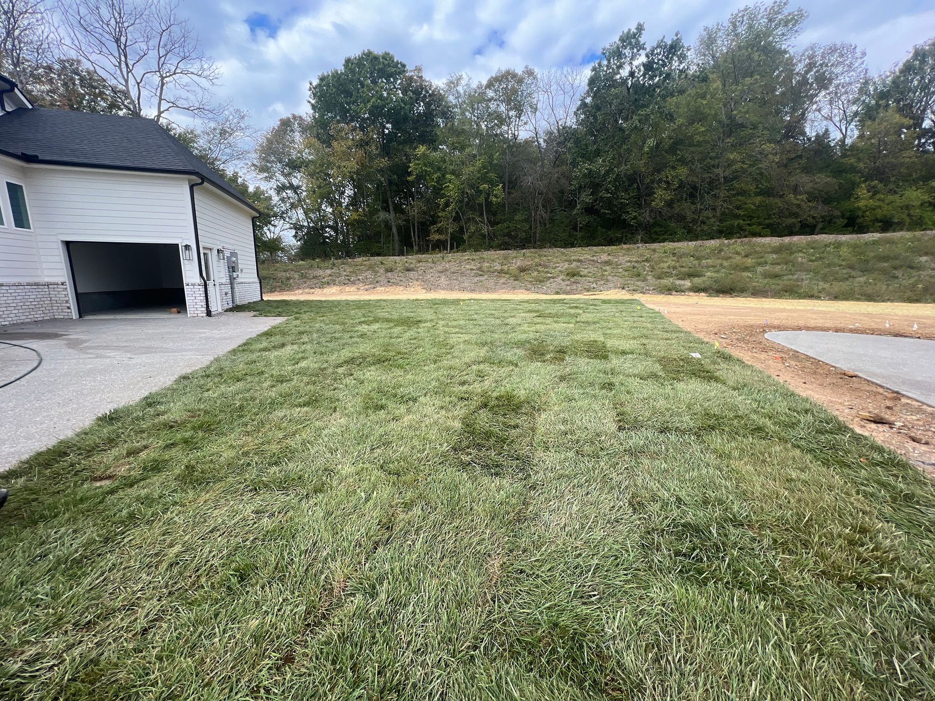 A large lawn with a garage in the background and trees in the background.
