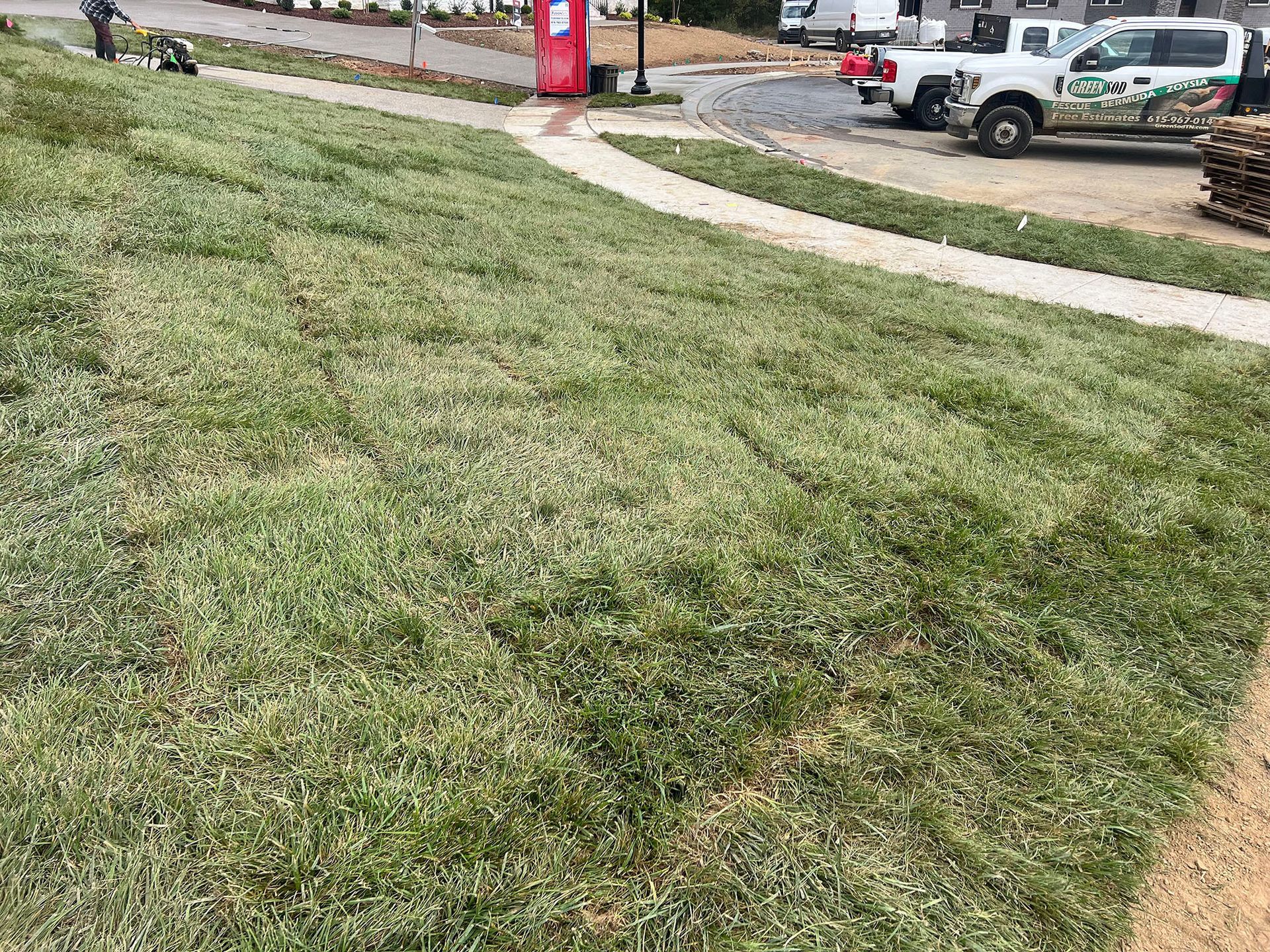 A lush green lawn with a sidewalk and a truck parked in the background.