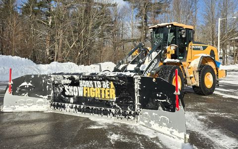 Yellow snowplow clearing a snow-covered parking lot with 