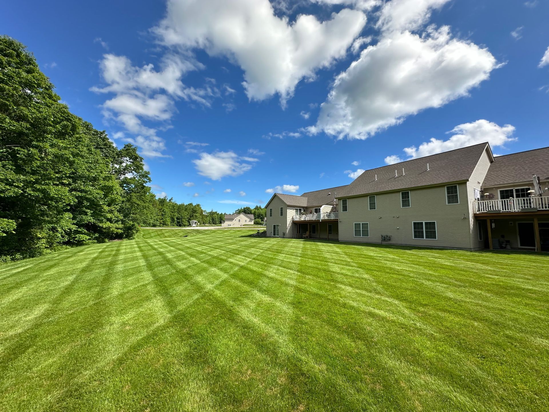 Lawn striped with mowing lines, two-story beige house under a blue sky with fluffy white clouds.