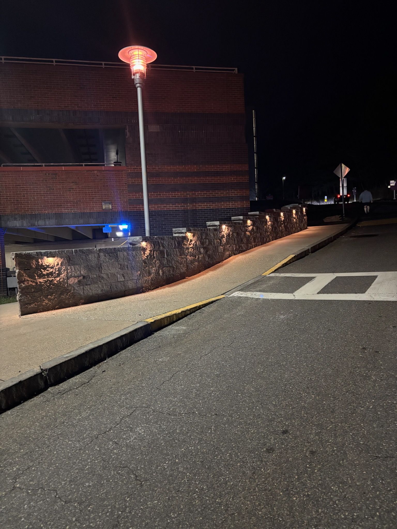 Brick building at night with lit wall, walkway, and street. A heat lamp glows overhead.