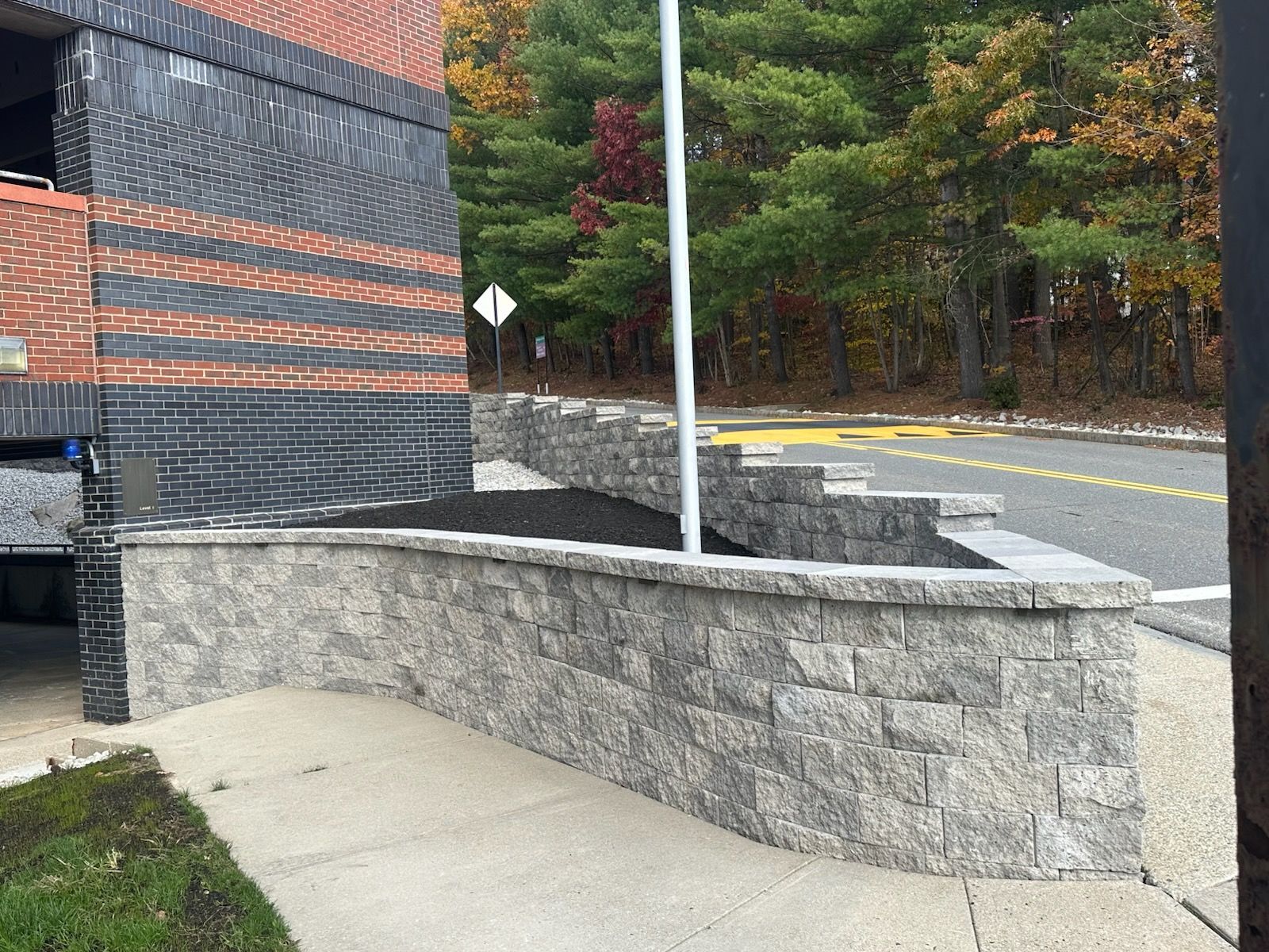 Building exterior with a stone retaining wall and black mulch, sidewalk, and roadway.