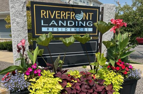 Sign for Riverfront Landing Residences, black with gold trim, surrounded by colorful flowers.
