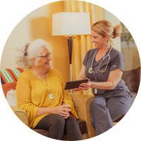 A nurse is sitting on a couch talking to an elderly woman.