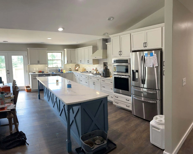 Spacious white kitchen with a blue island, stainless steel appliances, and a gray floor.