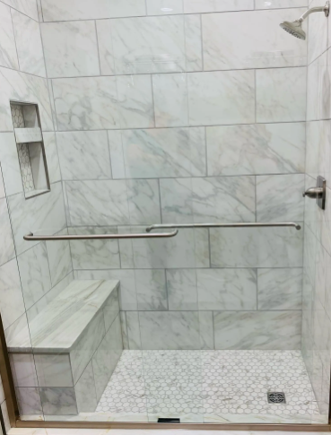 Modern shower with marble-like tiles, a built-in bench, and a glass door.