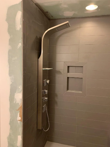 Gray tile shower with a modern silver shower panel and recessed shelf.